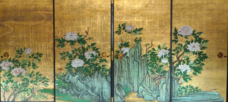 Zart blühende Päonien hinter einer Felsformation. Die Felsformation ist wie eine chinesische Penjing-Landschaft gestaltet. 